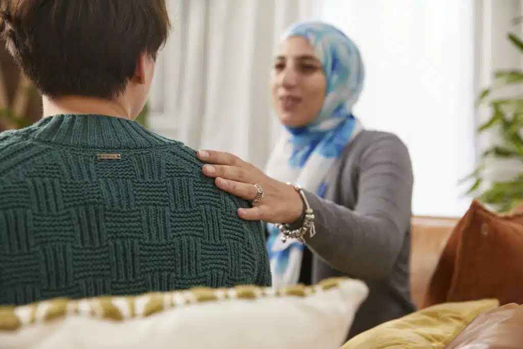 Woman on a leather couch talking to a man with her hand on his shoulder